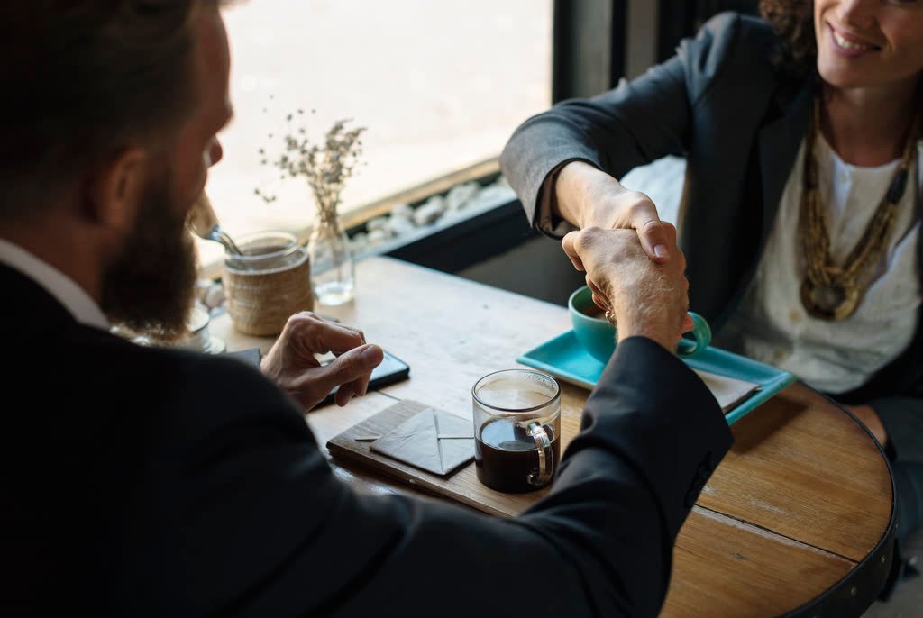 Deux personnes se serrent la main au-dessus d'une table, un accord vient d'être conclu
